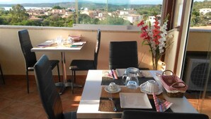 A balcony with a table set for breakfast, chairs, a vase with flowers, and a view of a town. - Antica Isola (Olbia)