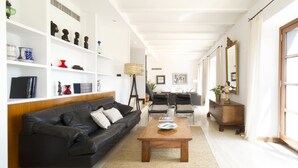 Una sala de estar moderna con un sofá de cuero negro, una mesa de centro de madera y estanterías blancas con objetos decorativos.