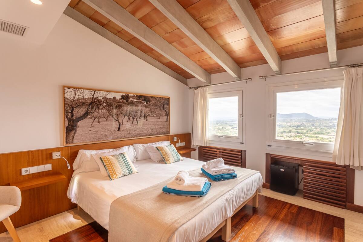 Une chambre d’hôtel avec un grand lit, un tableau au mur, une fenêtre donnant sur un beau paysage et un plafond en bois.
