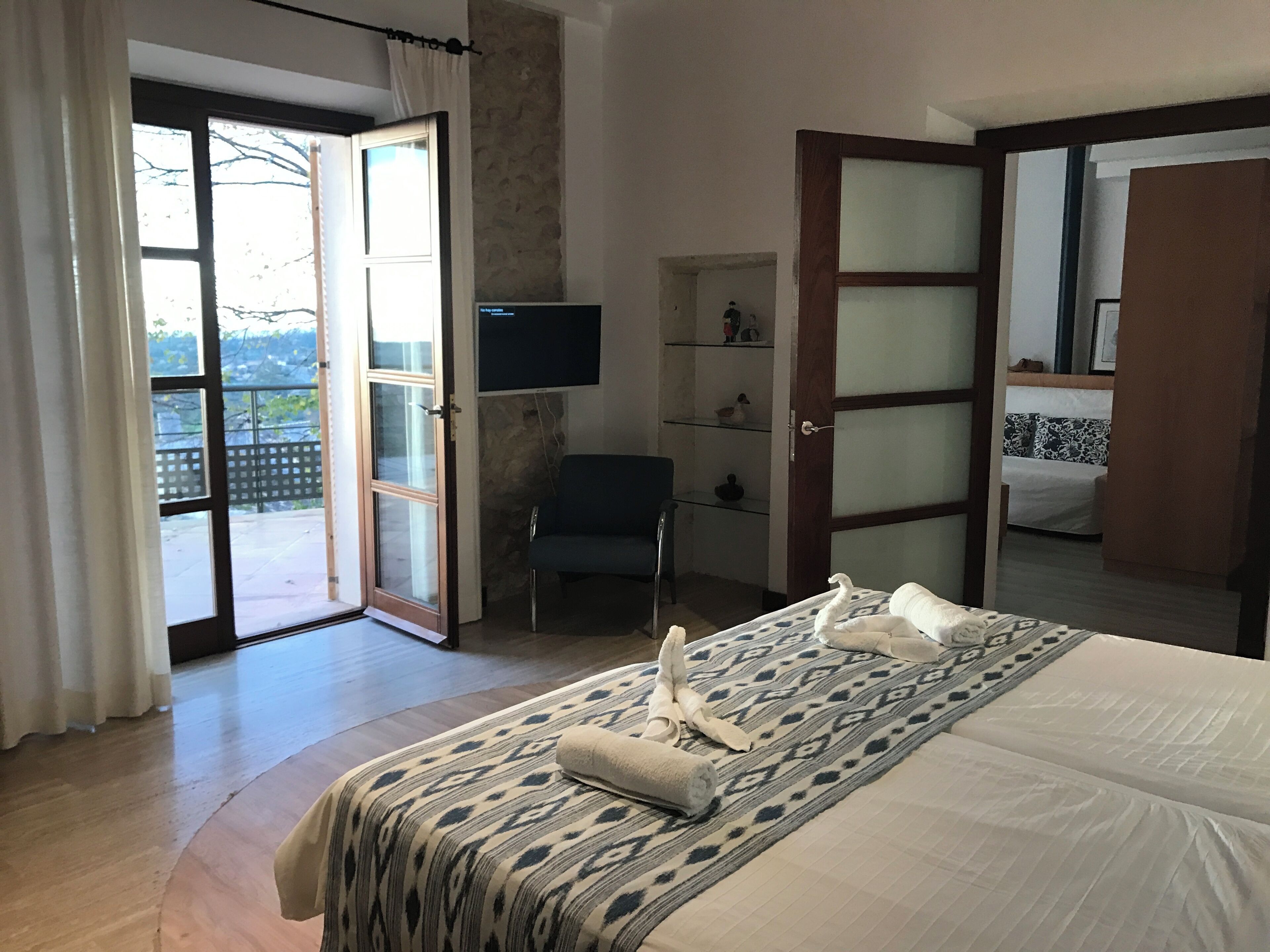 Habitación de hotel con cama, una silla, televisor y puerta corrediza de vidrio que da a un balcón.