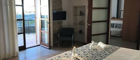 Habitación de hotel con cama, una silla, televisor y puerta corrediza de vidrio que da a un balcón.