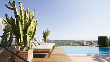 Una piscina al aire libre, sombrillas, sillones reclinables de piscina