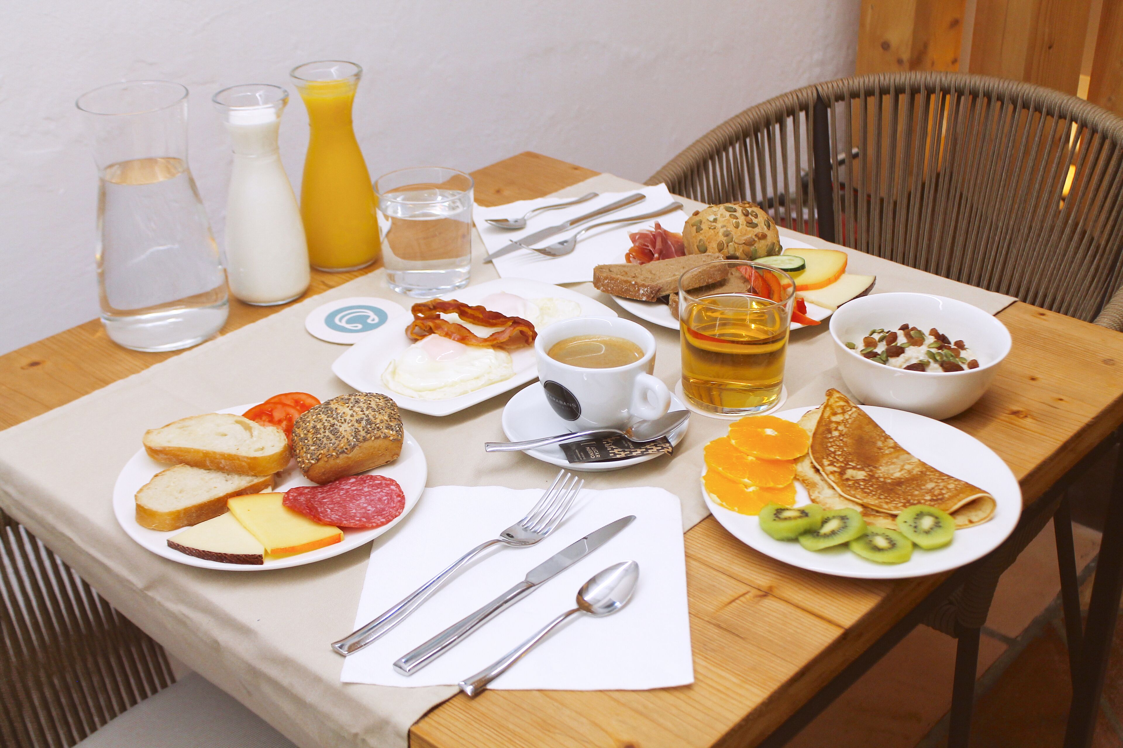 Uma mesa de café da manhã com diversos alimentos, utensílios e bebidas.