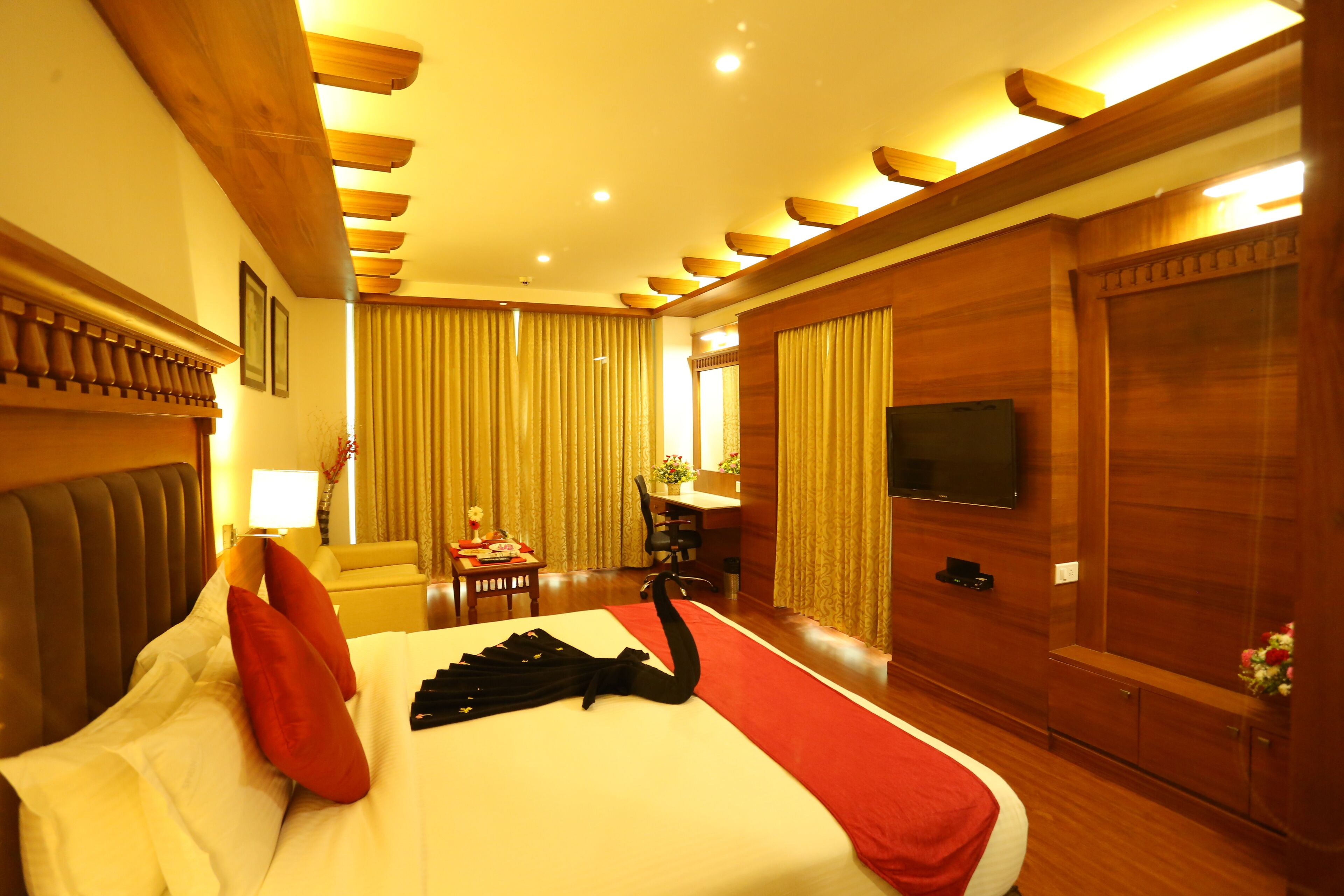 A hotel room with a large bed, a desk, a chair, a television, and wooden paneling.