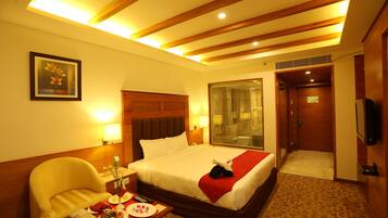 A hotel room with a bed, a chair, a bedside table with a lamp, a shower area, and a television.