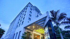 Una entrada de hotel moderna con un amplio frente de vidrio, un área de recepción cubierta y una escalera que conduce al vestíbulo.