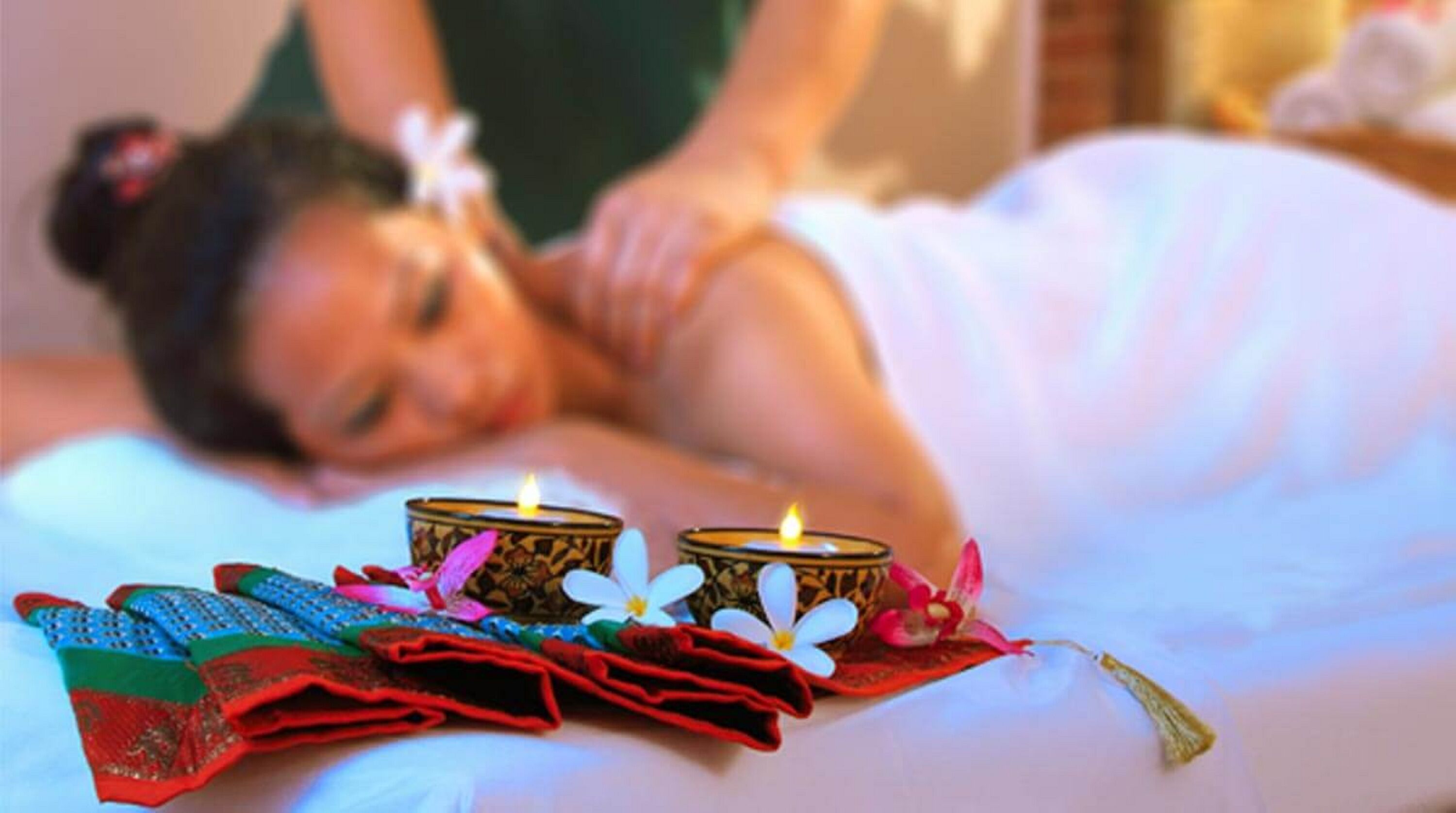 A person lying on a bed with candles and a decorative cloth.