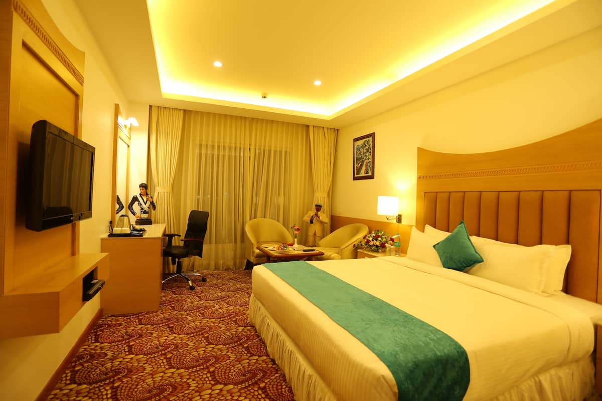 A hotel room with a large bed, a desk with a chair, a television, and a window with curtains.
