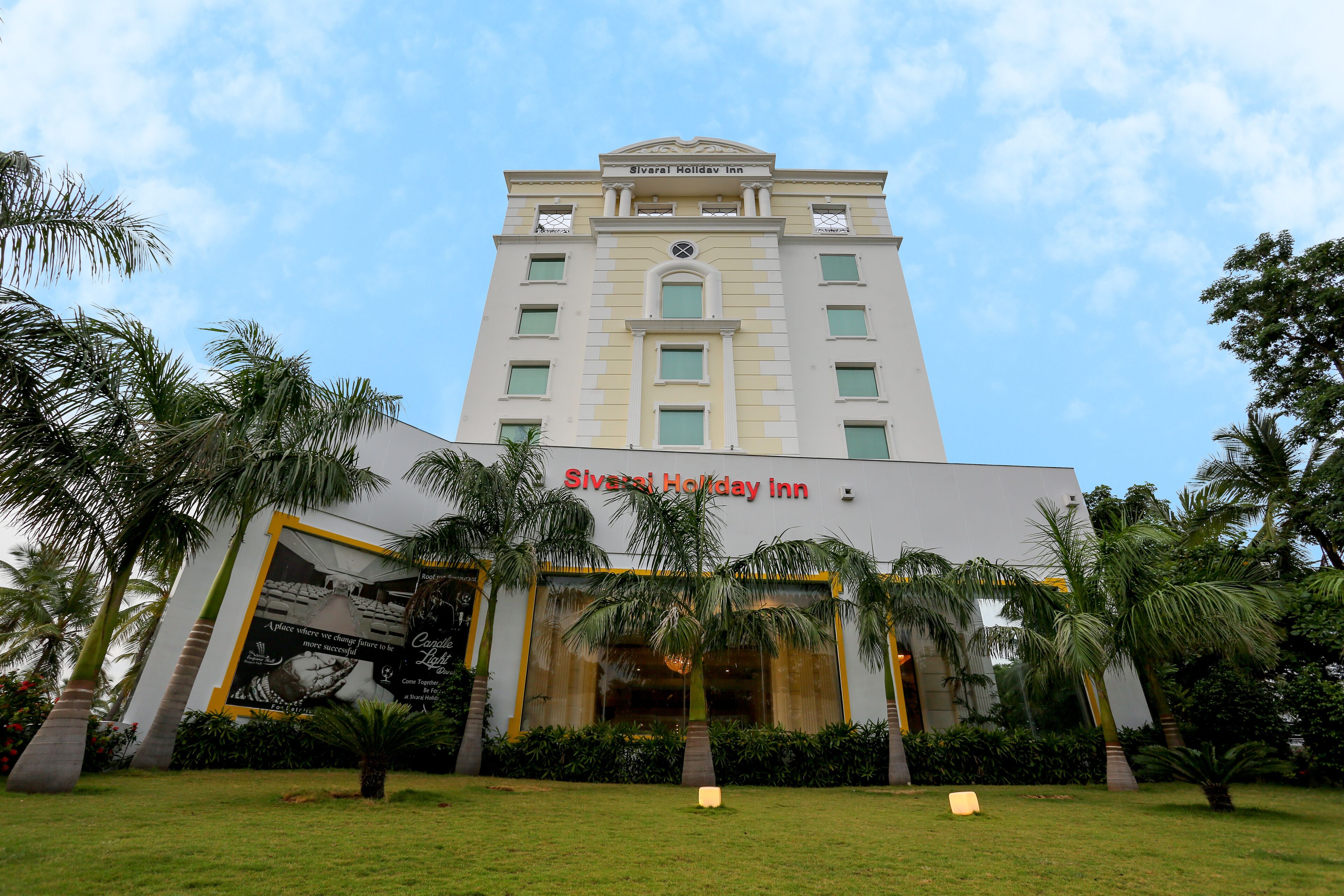 The exterior of the Silvarai Holiday Inn with a prominent entrance, surrounded by palm trees and a well-maintained lawn.