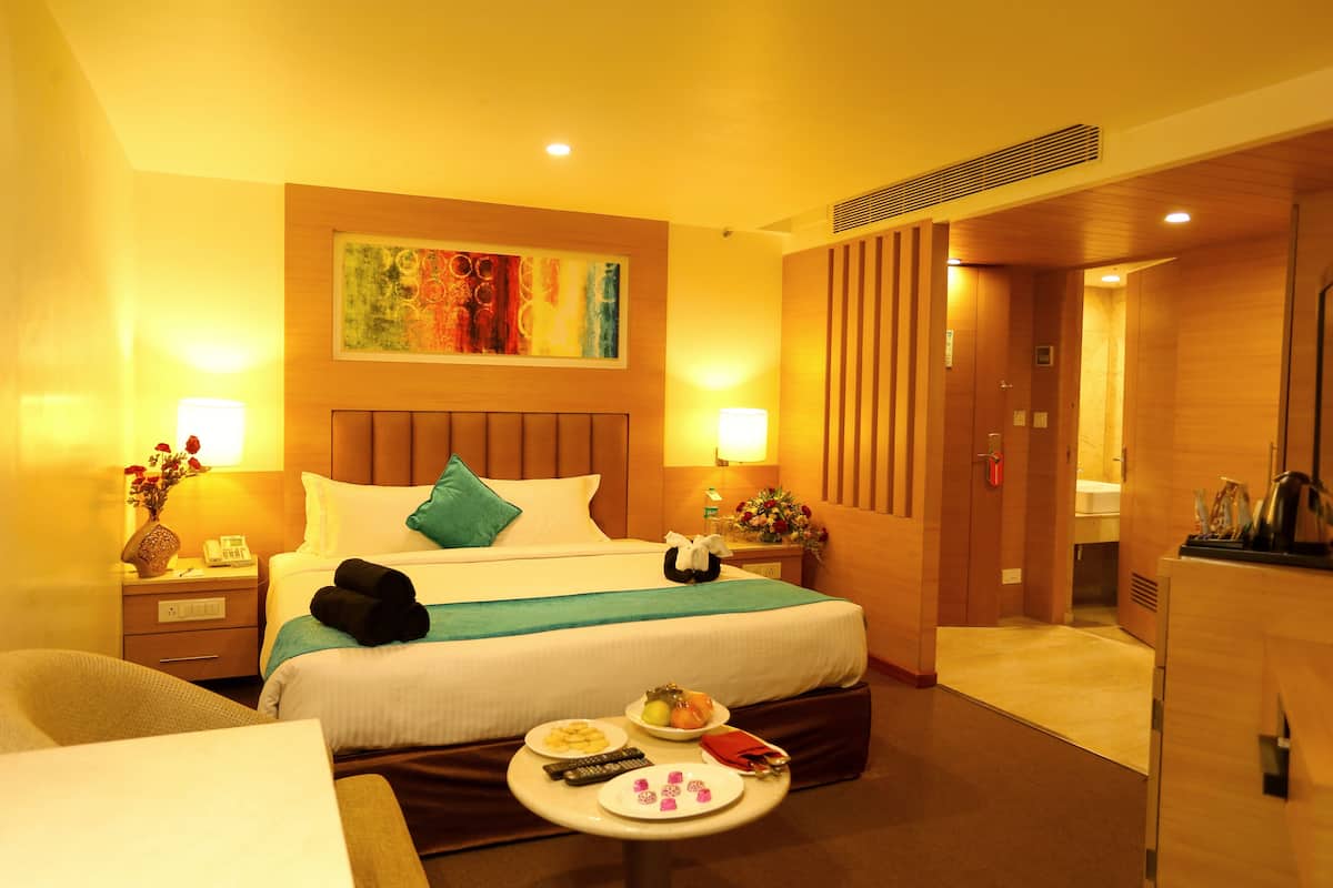 A hotel room with a bed, bedside tables, a small table with breakfast items, and a painting on the wall.