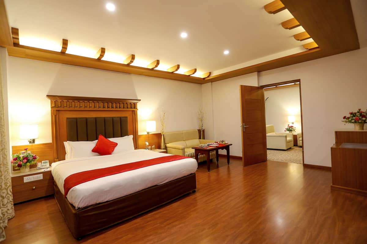 A hotel room with a large bed, bedside tables, a desk, a sofa, and a mirror.