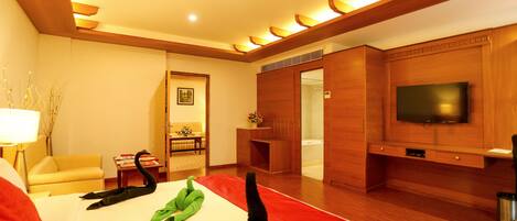 Habitación de hotel con cama, televisión, sofá y baño visible a través de una puerta abierta.