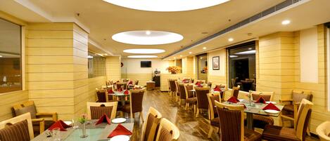A spacious dining area with multiple tables and chairs, a central service counter, and a modern ceiling design.