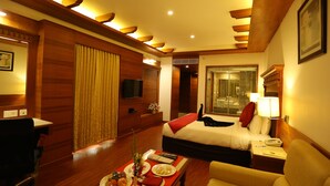 Habitación de hotel con cama, escritorio, silla, televisión y baño visible a través de una puerta de cristal.