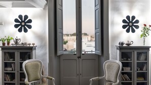 A room with a large window, two chairs, a cabinet with books, and a decorative flower on the wall.