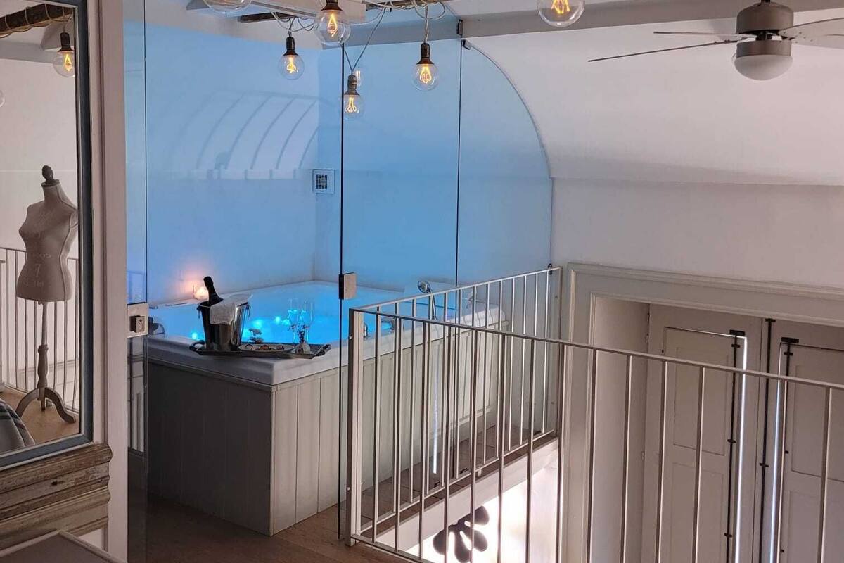 Un intérieur moderne avec des poutres apparentes, une cuisine à murs de verre et un balcon doté d’une rambarde en métal.