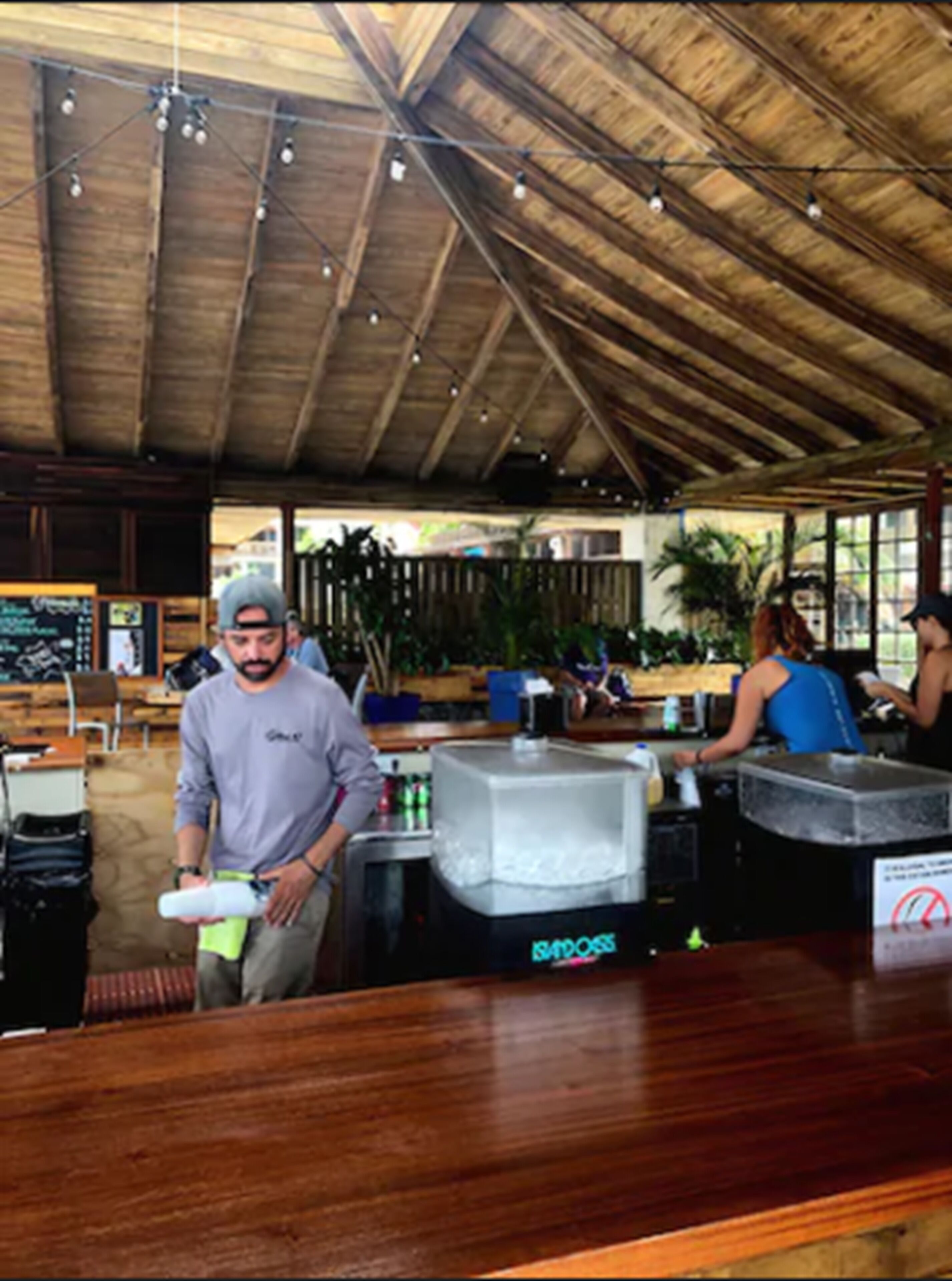 A bar area with a wooden ceiling, bar stools, and a counter with a large ice dispenser.