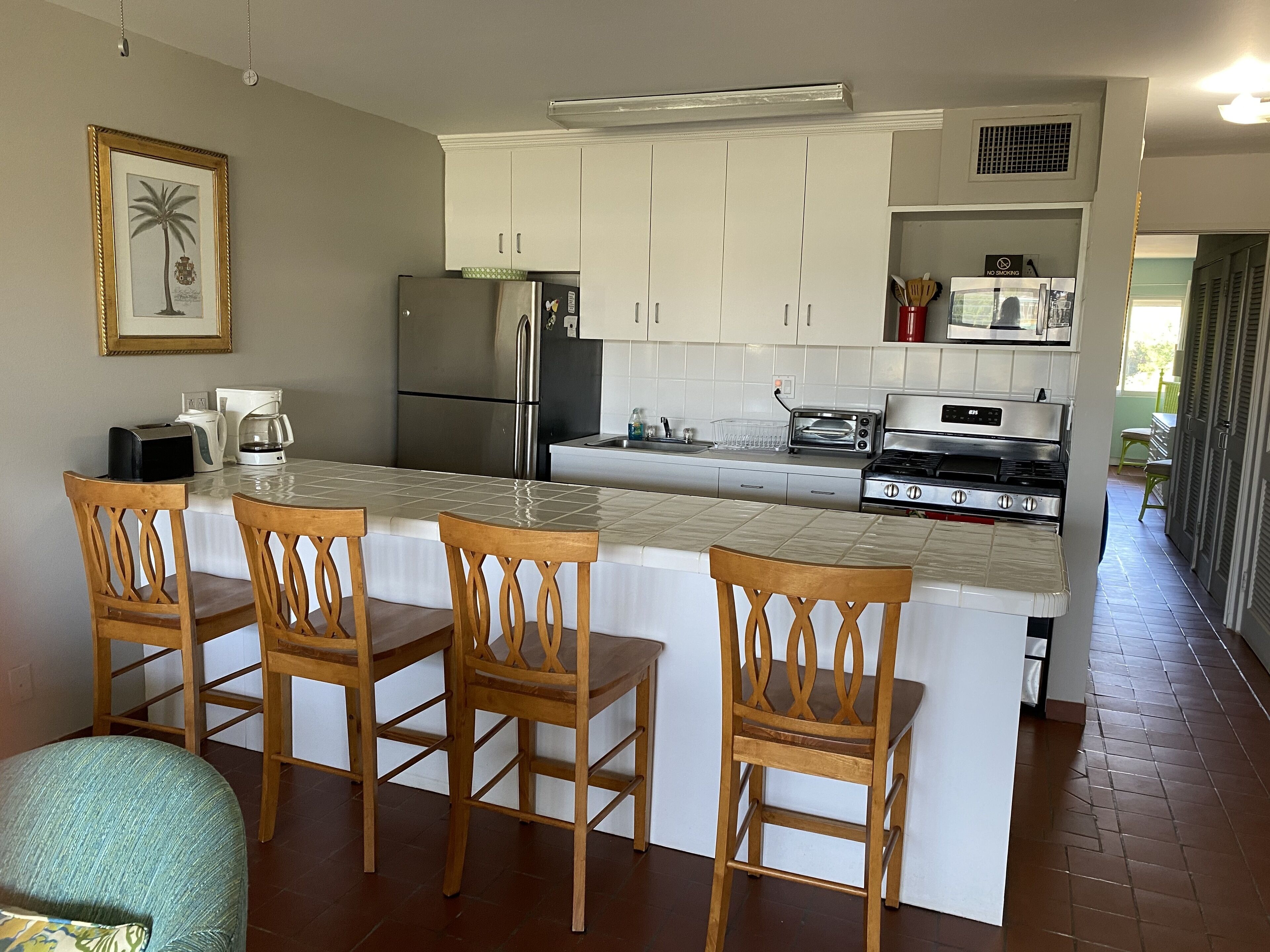 A kitchen with white cabinets, a stainless steel refrigerator, a stove, and a microwave. There are three wooden chairs at the island.
