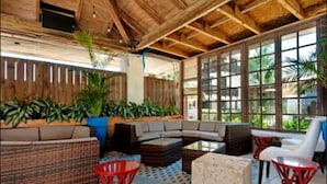 A covered outdoor seating area with a wooden ceiling, large windows, and potted plants.