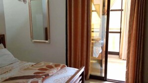 A bedroom with a bed, a mirror, and a sliding glass door leading to a balcony. - Residence Les Calanques (Dakar)