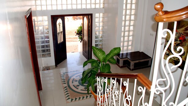 A staircase with a wooden handrail and white balusters, leading to a room with a patterned floor and a potted plant. - Residence Les Calanques (Dakar)