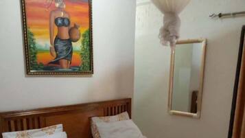A bedroom with a wooden bed, a painting on the wall, a mirror, and a canopy over the bed.