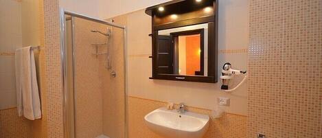 A bathroom with a glass shower enclosure, a white sink, and a mirror with a black frame.