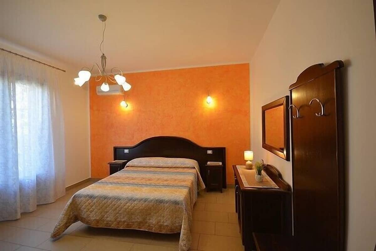 A hotel room with a bed, a desk, a chair, a mirror, and a chandelier.