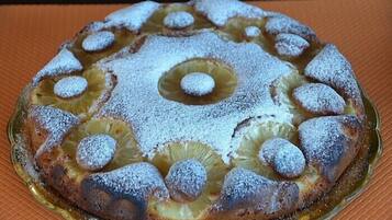 Een ronde cake met ananasschijfjes en poedersuiker op een glazen schaal.