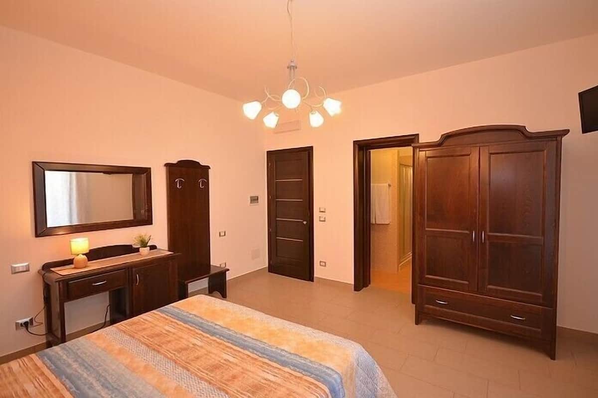 A bedroom with a bed, dresser, wardrobe, and a mirror.
