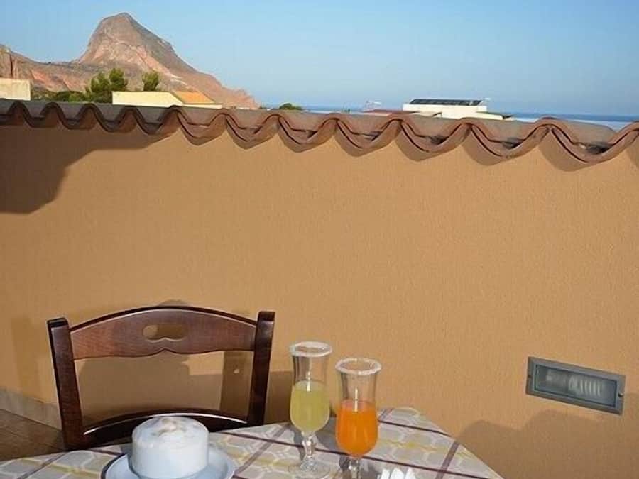 A table set with breakfast including a croissant, a small dish of fruit, a glass of orange juice, and a cup of coffee, with a view of the sea and mountains in the background.