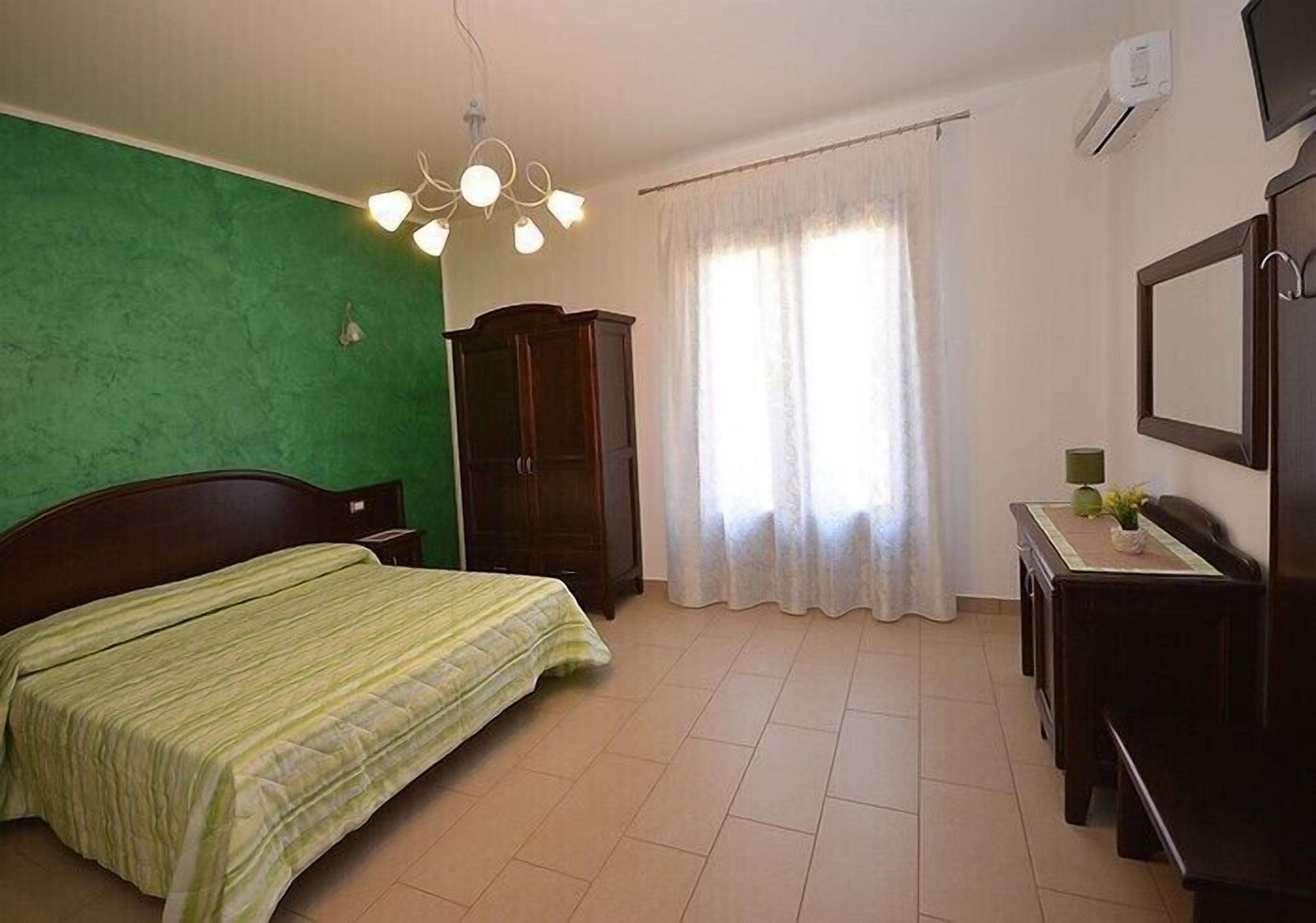 A bedroom with a bed, a wooden wardrobe, a desk with a chair, and a television.