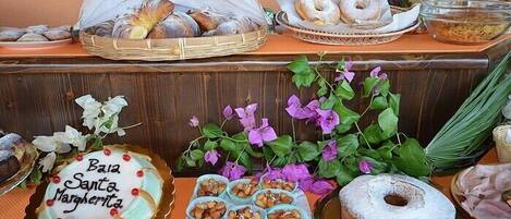 Una mesa de buffet con diversas opciones de panadería, incluyendo un pastel que dice 'Bia Santa Margarrita', y una variedad de pasteles y pan.