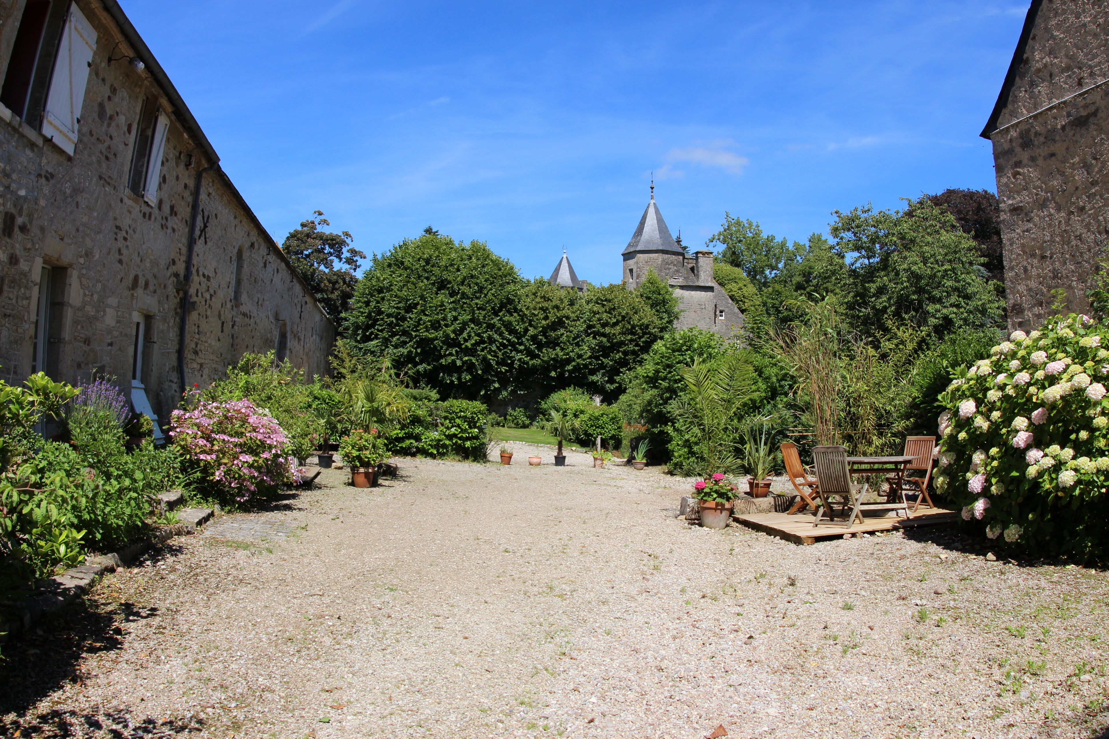 A courtyard with a gravel path, potted plants, and outdoor furniture.