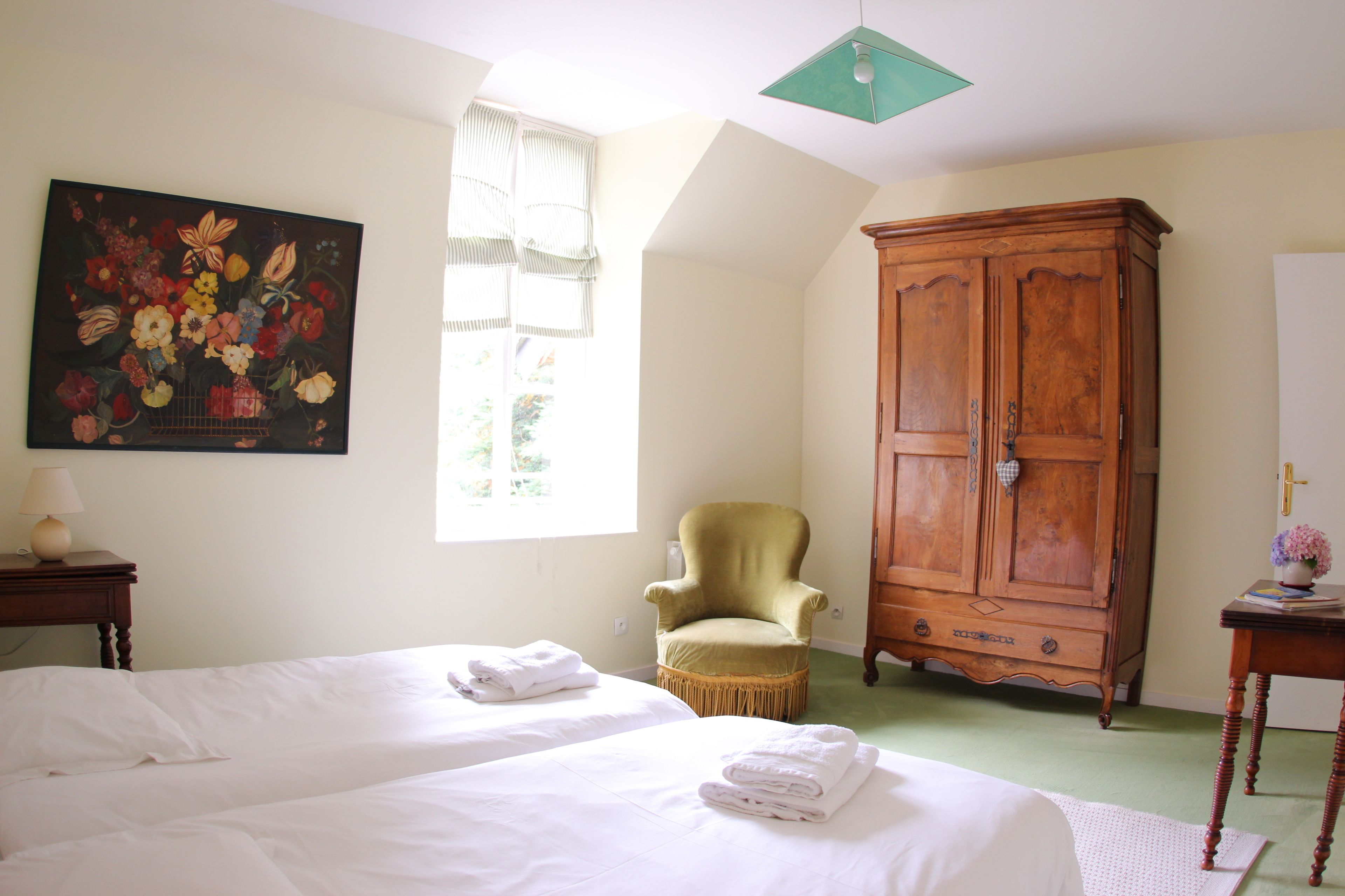Une pièce avec deux lits, une grande armoire en bois, un fauteuil vert et un tableau accroché au mur.