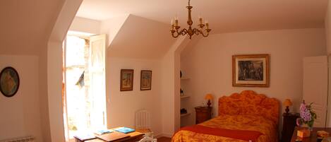 A bedroom with a large bed, a desk, and a chair. There is a chandelier hanging from the ceiling.