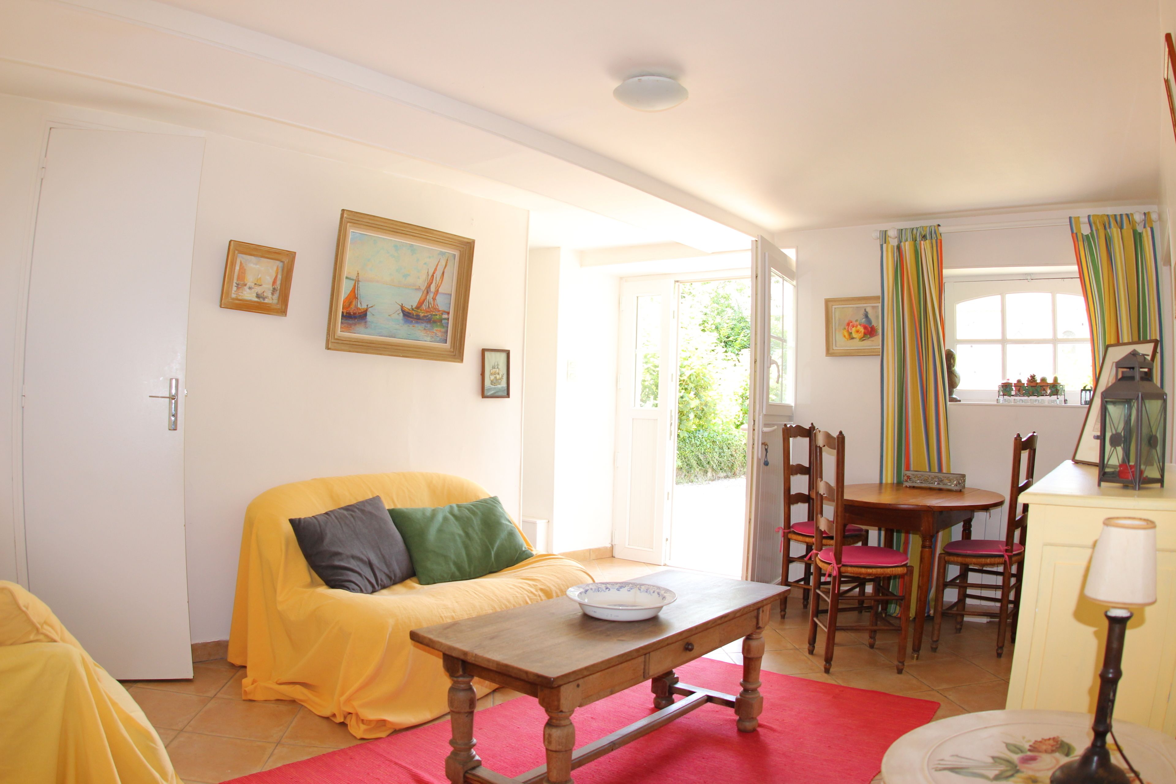 A cozy living room with a yellow sofa, a wooden table, and a dining area with chairs.