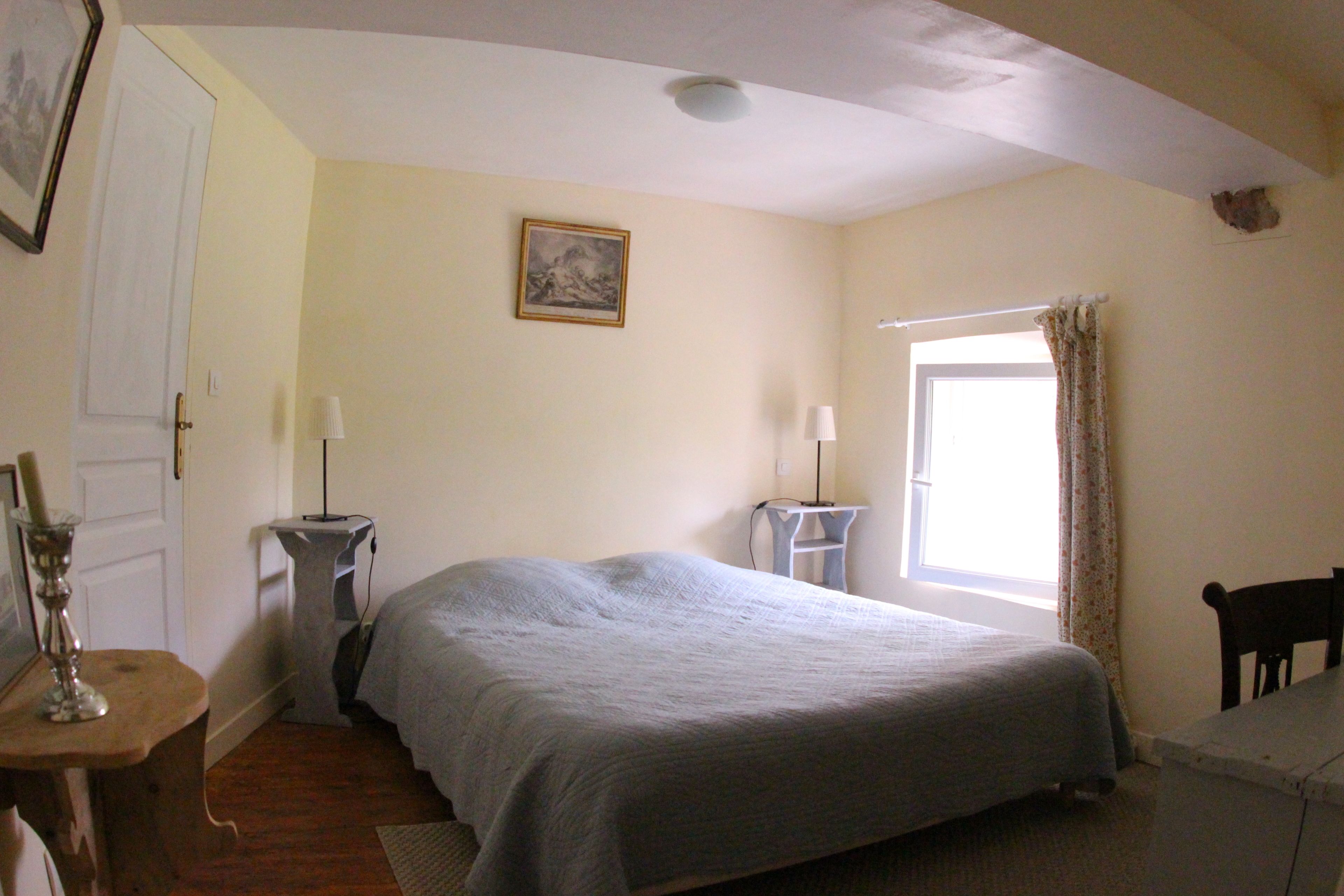 A bedroom with a bed, bedside tables, a window with curtains, a door, and a painting on the wall.