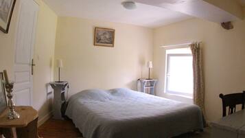 A bedroom with a bed, bedside tables, a window with curtains, a door, and a painting on the wall.