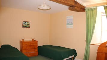 Una habitación con dos camas individuales, un aparador de madera, un cuadro pequeño en marco y una ventana con cortinas verdes.