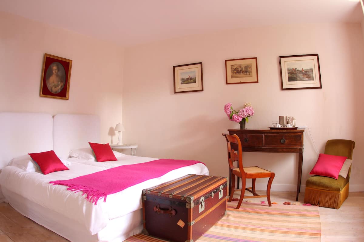 Un dormitorio con cama, un escritorio, una silla, una maleta y cuadros en la pared.