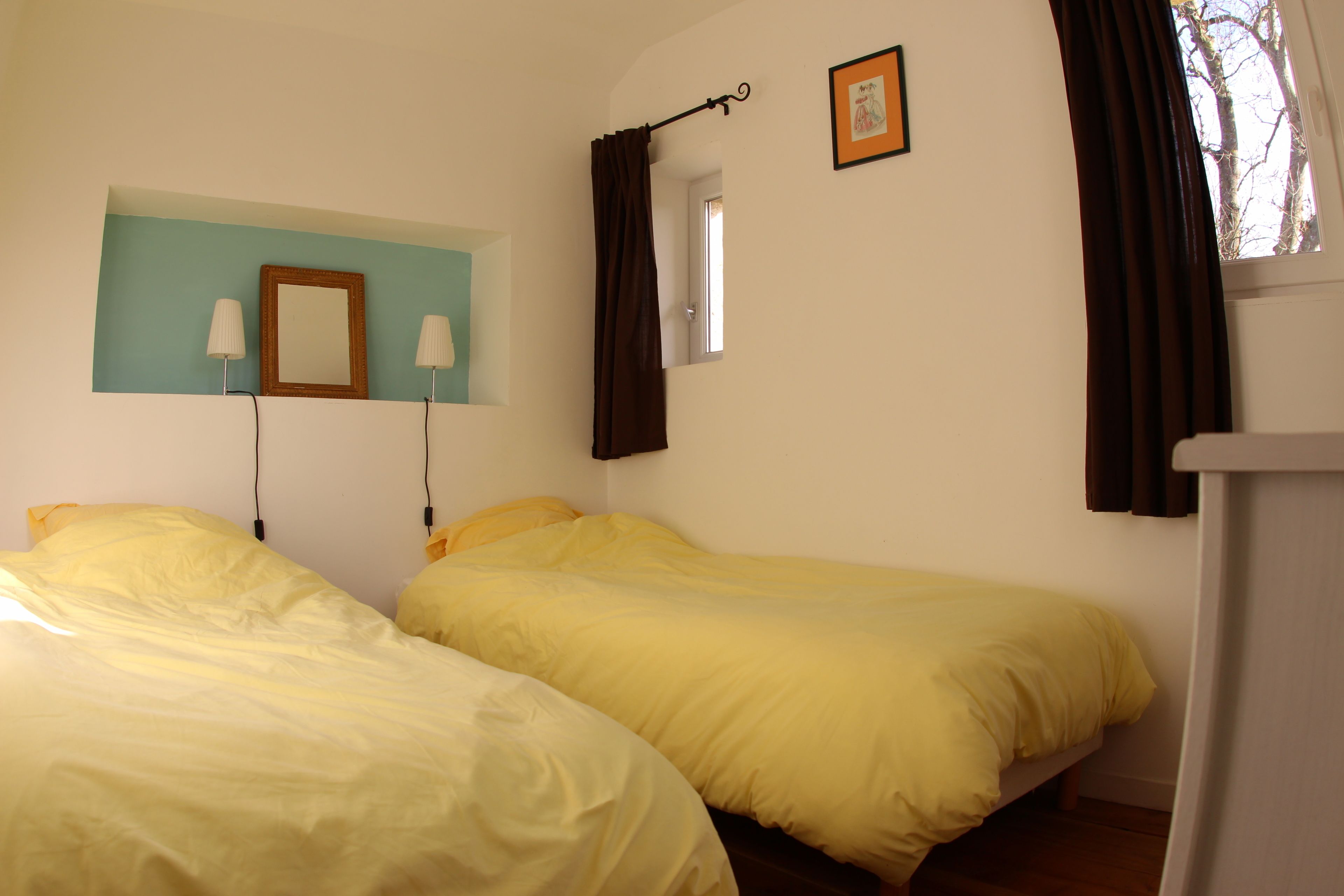 Een kamer met twee bedden, een raam met gordijnen, een spiegel en een foto aan de muur.