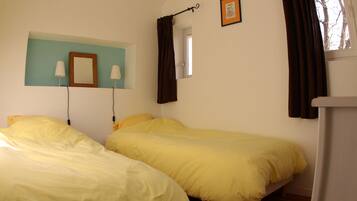 Een kamer met twee bedden, een raam met gordijnen, een spiegel en een foto aan de muur.
