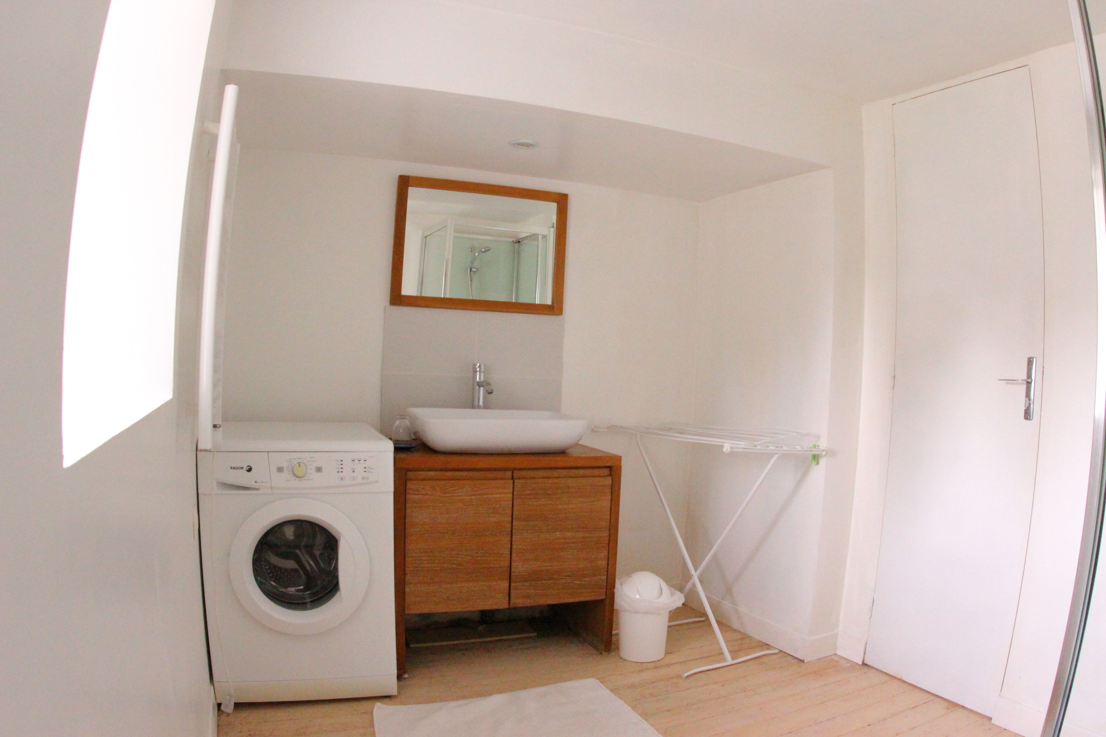 A small, clean bathroom with a washing machine, wooden vanity, and a mirror above the sink.