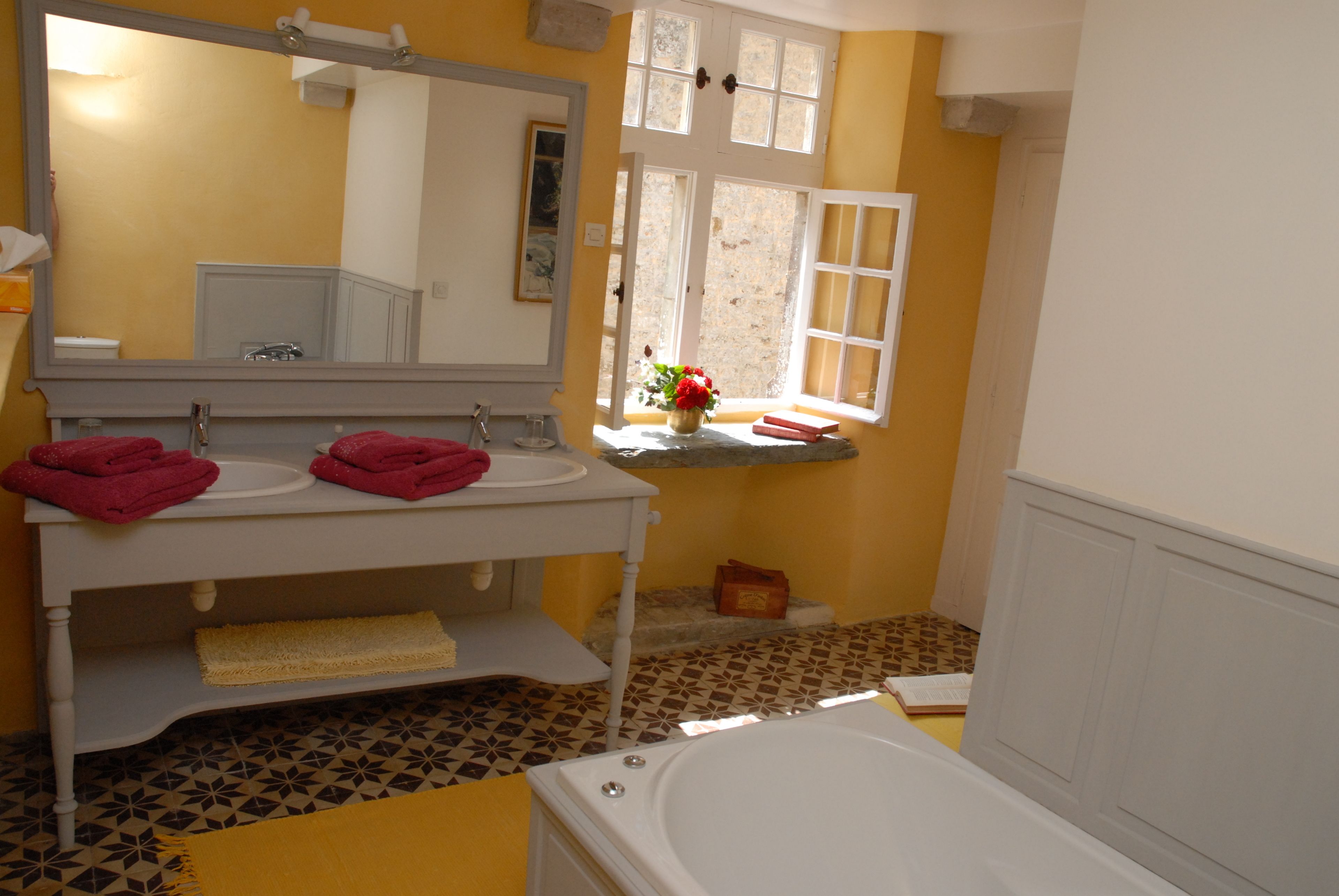 Une salle de bain avec une baignoire, un meuble-lavabo avec un miroir et une fenêtre donnant sur l’extérieur.