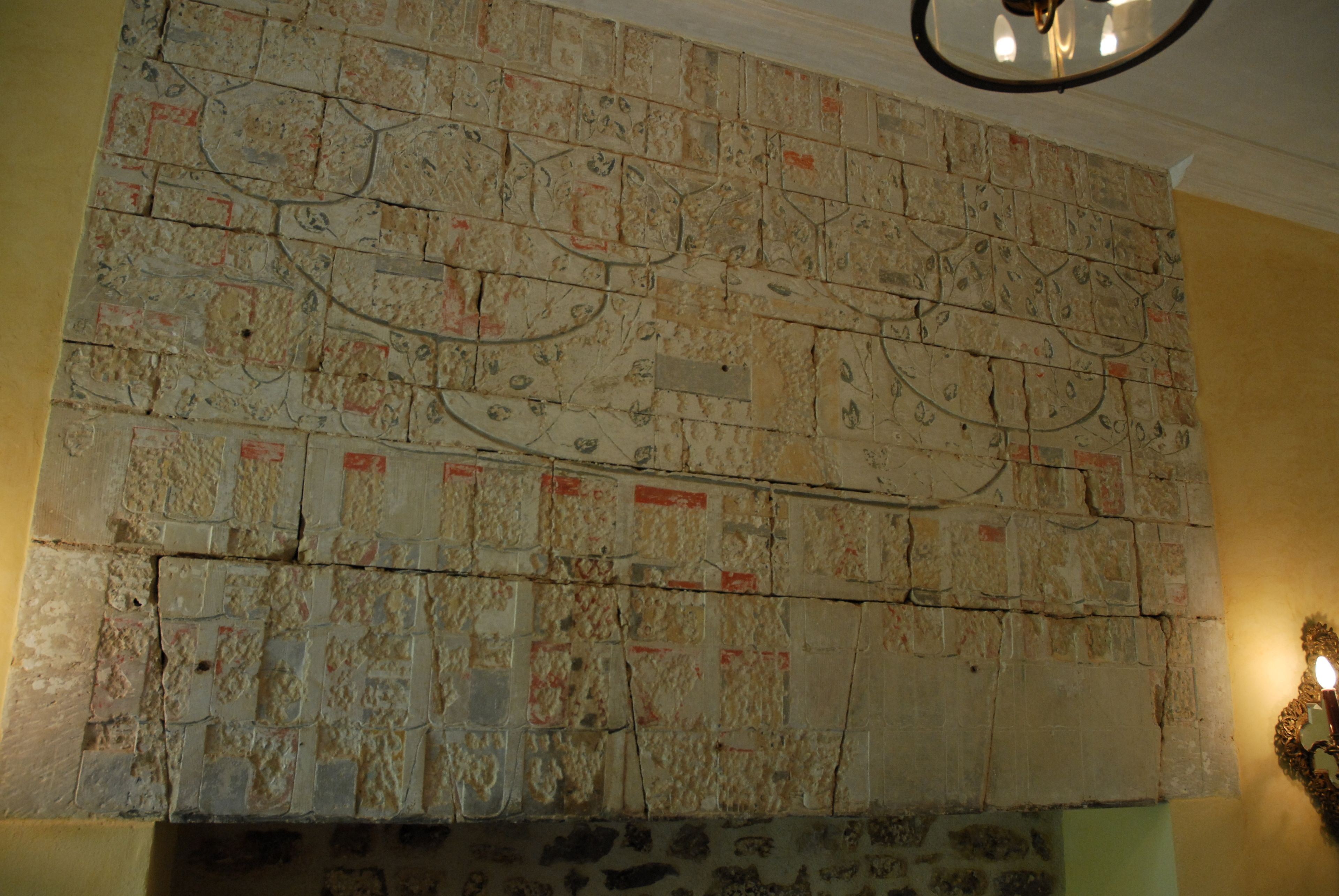 Un mur en pierre orné d’un motif décoratif, une cheminée en pierre et un luminaire fixé au mur.