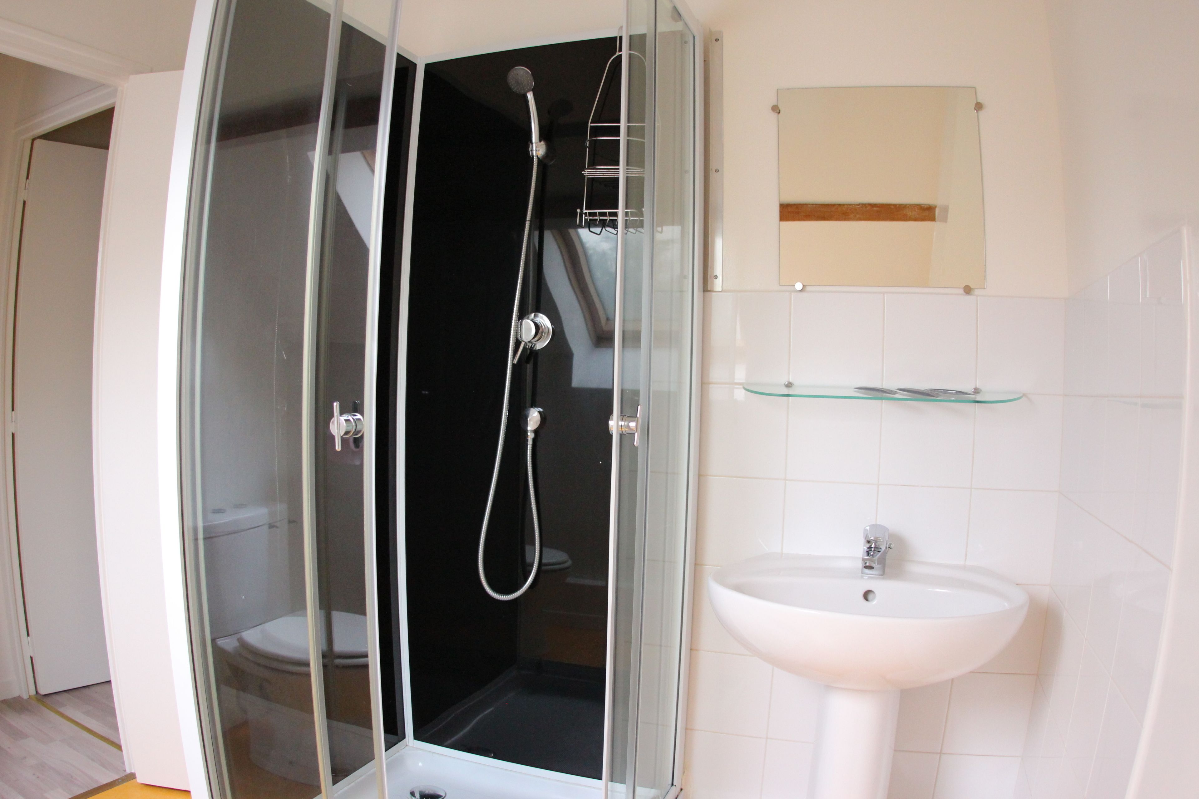 Un baño con ducha acristalada, un lavamanos blanco y un espejo sobre el lavabo.