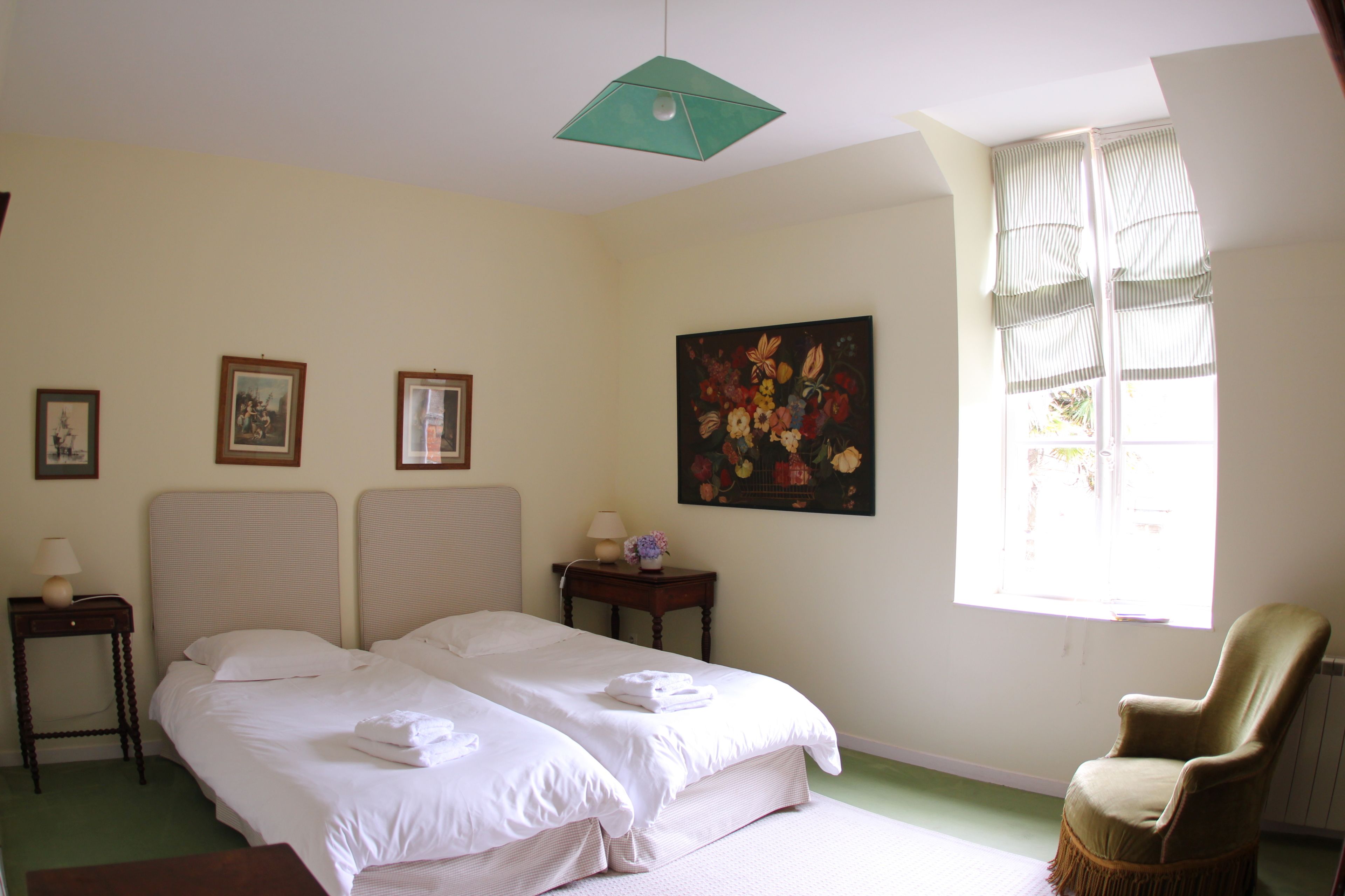 A hotel room with two beds, a chair, a painting, and a window with curtains.