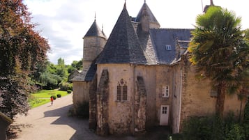 A historic building with a gravel path leading to the entrance, surrounded by lush greenery and a clear sky.