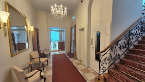 A hotel lobby with a chandelier, a mirror, a reception desk, and a staircase. - Hotel Beethoven (Frankfurt)